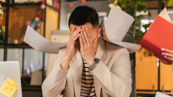 Exhausted Bangladeshi professional sitting at desk with hand on forehead, symbolizing burnout and mental fatigue.